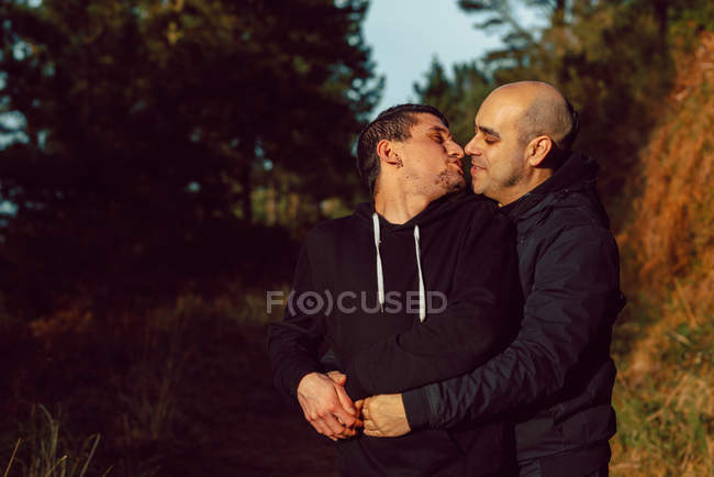 Гомосексуальна пара обіймає і цілує на прогулянці в лісі в сонячний день на розмитому фоні — стокове фото