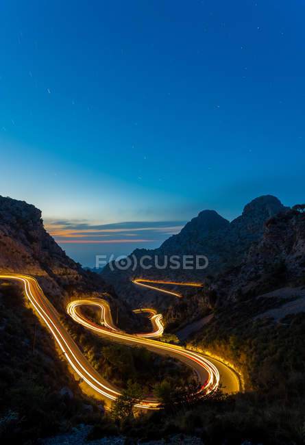 Exposição longa de luzes de trilha à noite entre montanhas — Fotografia de Stock