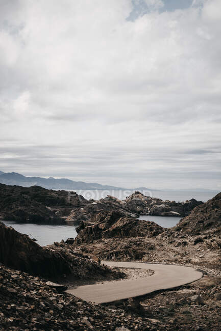Route goudronnée étroite traversant une magnifique plage de rochers rugueux près de la montagne — Photo de stock