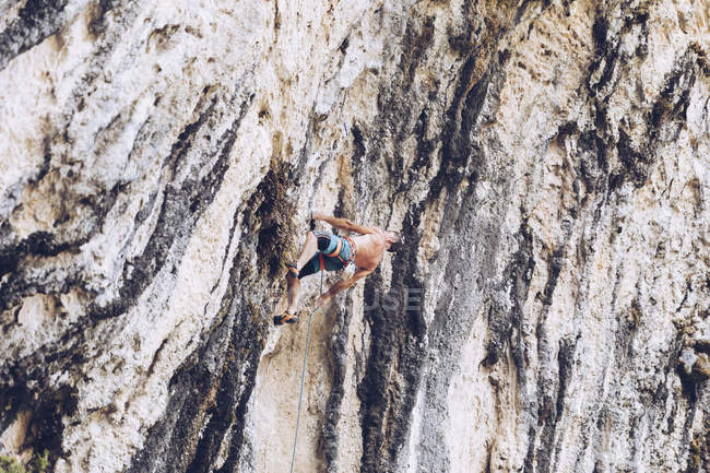 Side view of unrecognizable male in shorts climbing up rough cliff on sunny day in countryside — Stock Photo