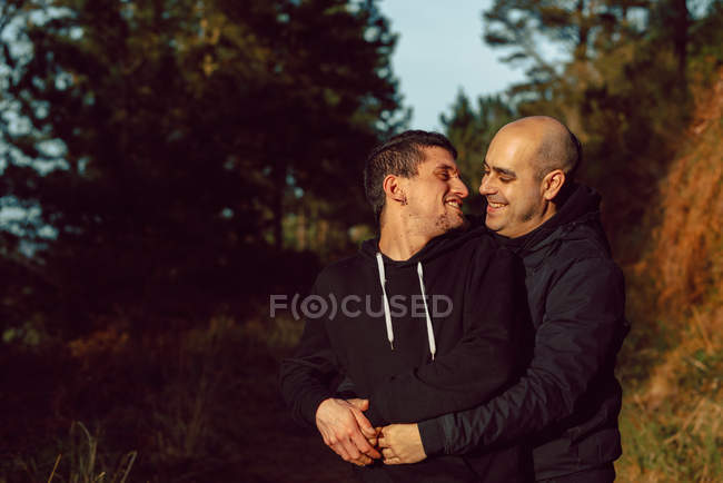 Гомосексуальна пара обіймає і цілує на прогулянці в лісі в сонячний день на розмитому фоні — стокове фото