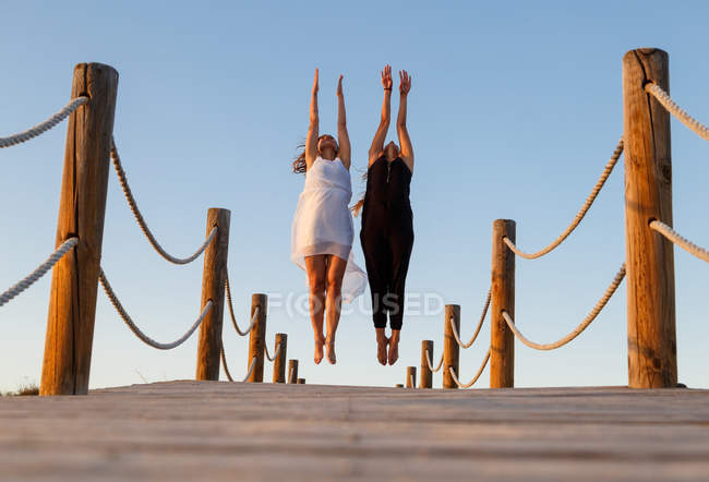 Молоді балерини в чорно-білому одязі з посиленими руками в повітрі на пішохідному мосту і блакитним небом в сонячний день — стокове фото