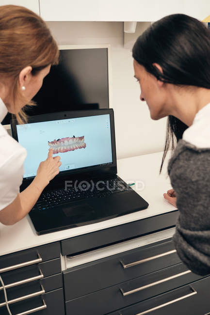 Dentista feminino demonstrando laptop com varredura de dentes para a mulher na clínica — Fotografia de Stock