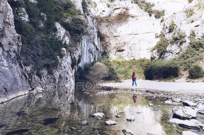 Visão traseira da mulher com mochila na costa do rio da montanha perto da montanha de rocha — Fotografia de Stock