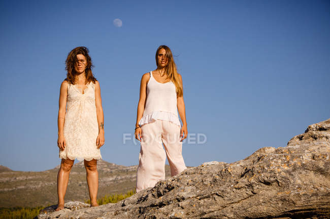 Jeunes femmes mystérieuses posant sur des rochers près de la colline et le ciel bleu avec la lune — Photo de stock