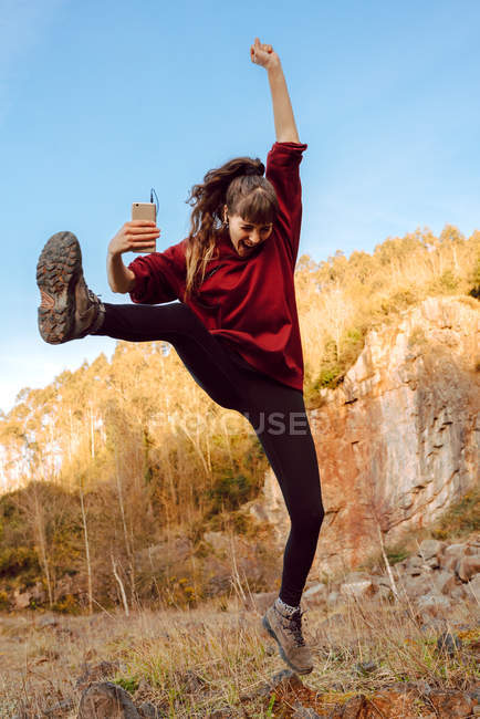 Young hipster woman with upped hand listening music on mobile phone and dancing in nature — Stock Photo