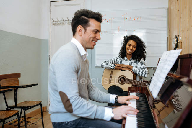 Сторона зору молодого чоловіка, який грає на фортепіано поруч з чорношкірою жінкою, граючи на гітарі в музичній студії — стокове фото