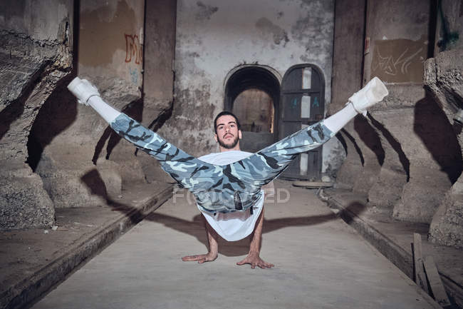 Attractive young man performing difficult dance movement near weathered columns of aged building — Stock Photo
