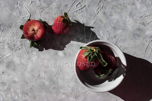 Fresh strawberries in bowl and on grey surface — Stock Photo