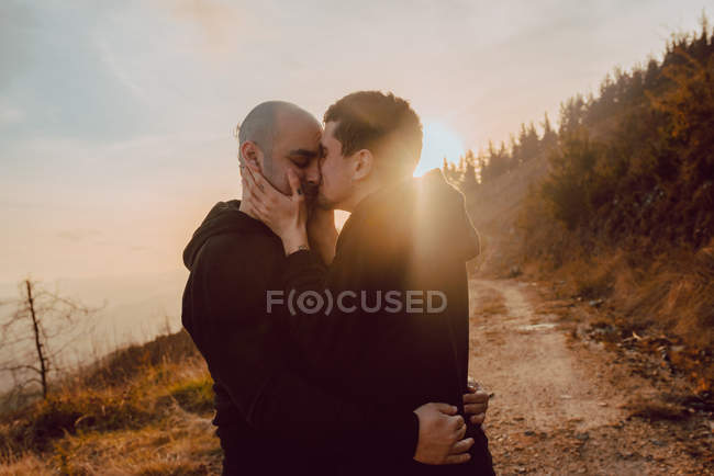 Счастливая гомосексуальная пара обнимается и целуется в лесу в солнечный день — стоковое фото
