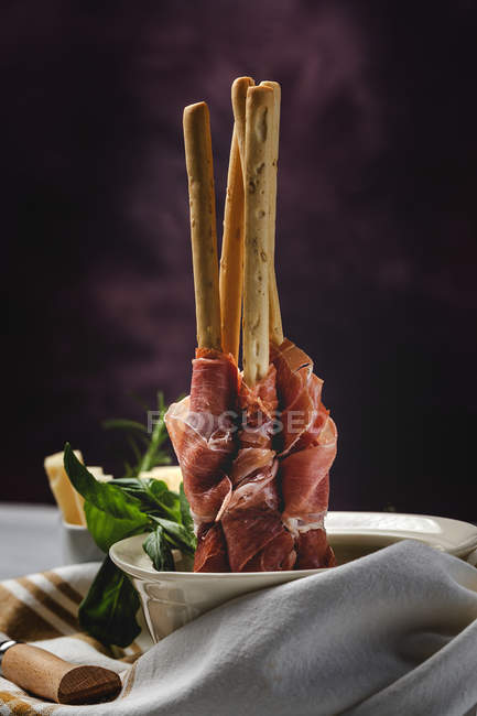 Gressini con tipico prosciutto serrano spagnolo in ciotola su fondo scuro — Foto stock