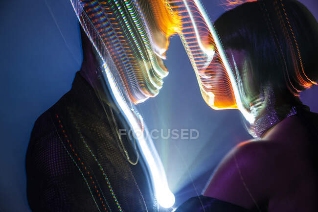 Traces lumineuses de lumière colorée sur les visages de jeune homme et femme sur fond bleu — Photo de stock