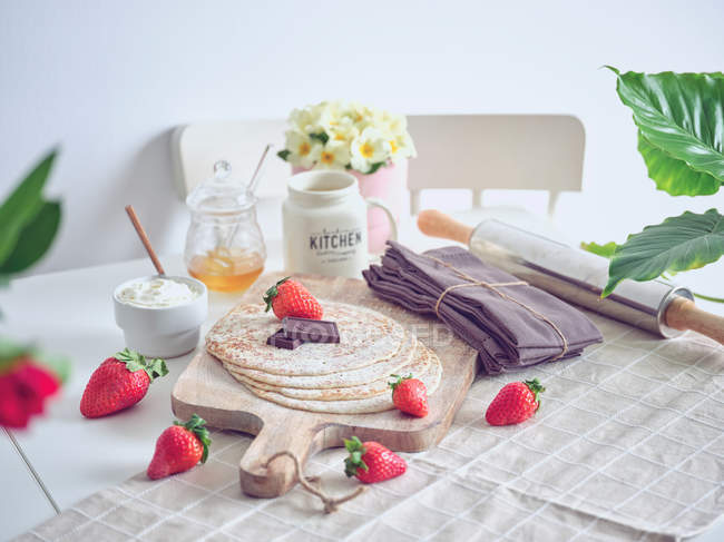 Desayuno con tortitas y fresas en la mesa de la cocina con flores - foto de stock