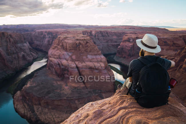 Back view of bearded guy with backpack looking at beautiful canyon and calm river on sunny day on West Coast of USA — Stock Photo