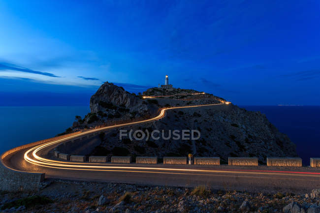 Довга експозиція легких стежок вночі з маяком на пагорбі — стокове фото