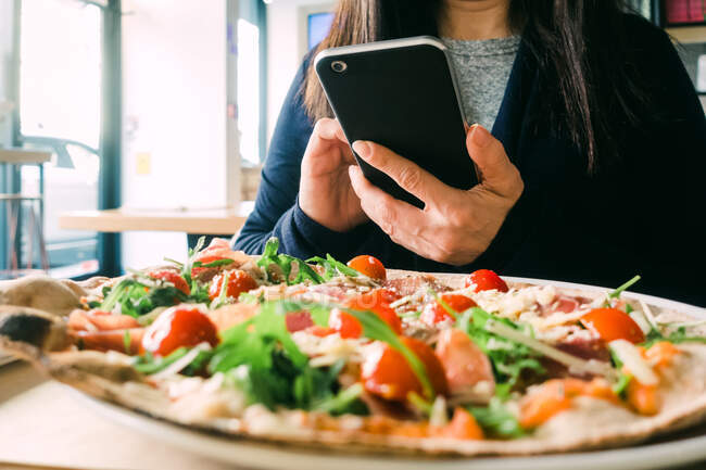 Обрізати жінку за допомогою мобільного телефону і сидіти за столом зі смачним салатом в кафе — стокове фото