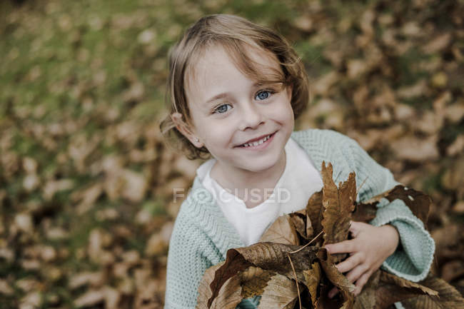 Amusant enfant tenant tas de feuillage sec dans le parc sur fond flou — Photo de stock