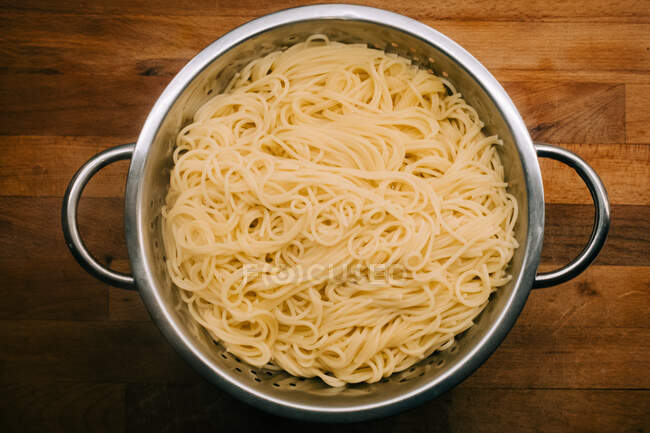Dall'alto spaghetti cucinati freschi in pentola d'argento su sfondo di legno — Foto stock