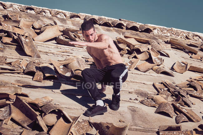 El hombre saltando en el viejo techo de mala calidad - foto de stock