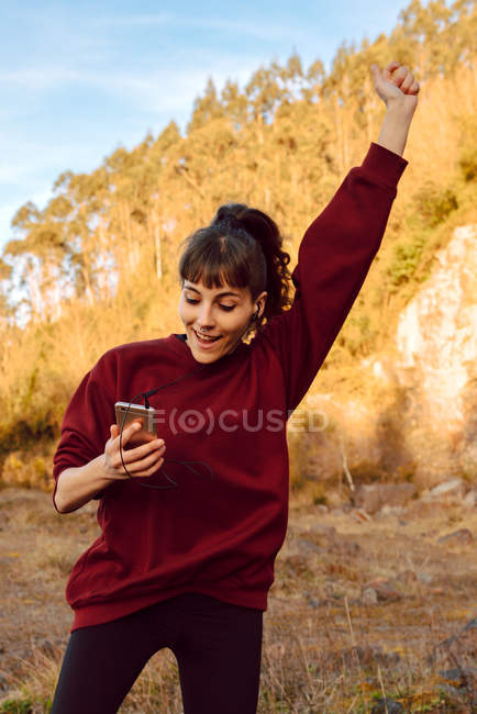 Junge Hipsterfrau mit erhobener Hand, die Musik auf dem Handy hört und in der Natur tanzt — Stockfoto