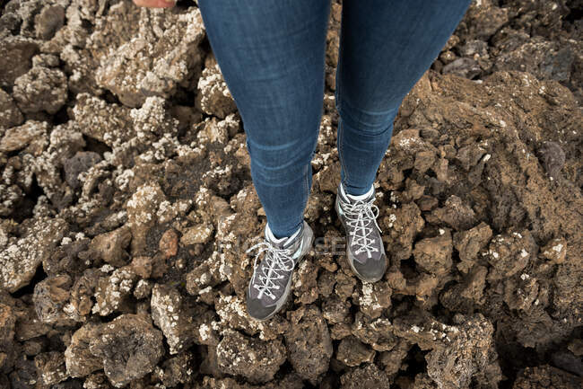 Зверху ноги анонімної жінки в джинсах і кросівках, що стоять на скелястій землі в сільській місцевості — стокове фото