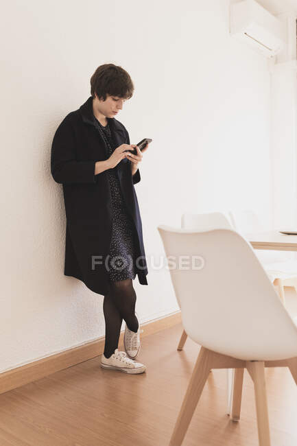Концентрированная юная леди с помощью мобильного телефона рядом со столом — стоковое фото