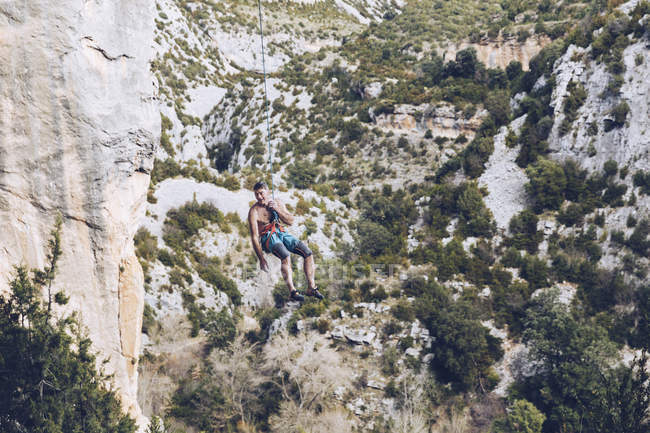 Снизу альпинист висит на веревке на грубой скале против голубого неба — стоковое фото