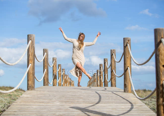 Junge Ballerina im Kleid tanzt auf Fußgängerbrücke unter blauem Himmel bei sonnigem Tag — Stockfoto