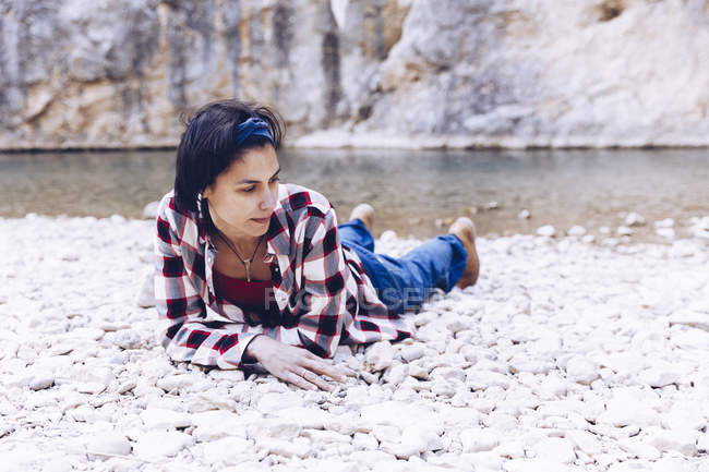 Молодая женщина лежит на скальном берегу горной реки возле скалы — стоковое фото