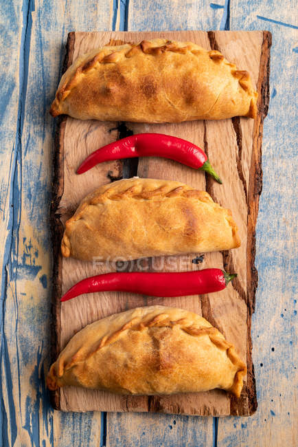 Hausgemachte gebackene Pasteten und frische rote Chilischoten auf Holzbrett — Stockfoto