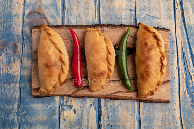 Hausgemachte gebackene Pasteten und frische rote und grüne Chilischoten auf Holzbrett — Stockfoto