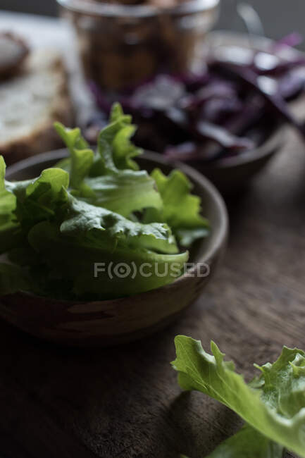Closeup folhas frescas de salada em tigela perto de pão no fundo de madeira — Fotografia de Stock