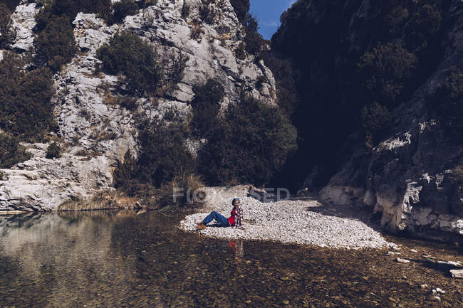 Young woman lying on rock coast of mountain river near cliff — Stock Photo
