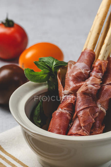 Gressinis with spanish typical serrano ham in white bowl with fresh tomatoes on background — Stock Photo