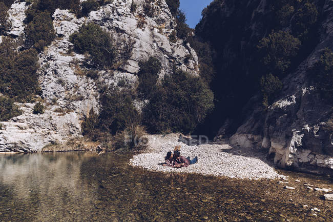 Vue latérale du jeune couple couché et embrassant sur la côte rocheuse de la rivière de montagne près de la falaise — Photo de stock