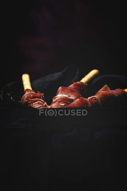 Gressinis com presunto serrano típico espanhol na placa no fundo escuro — Fotografia de Stock