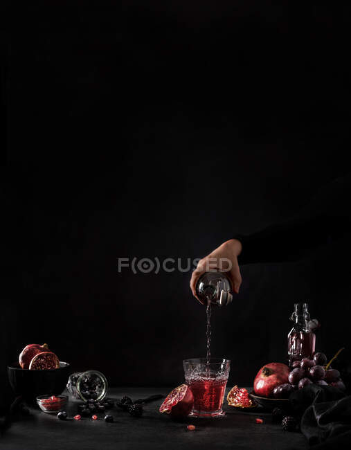 Рука с зерном наливает гранатовый сок из бутылки в стекло на черном фоне — стоковое фото