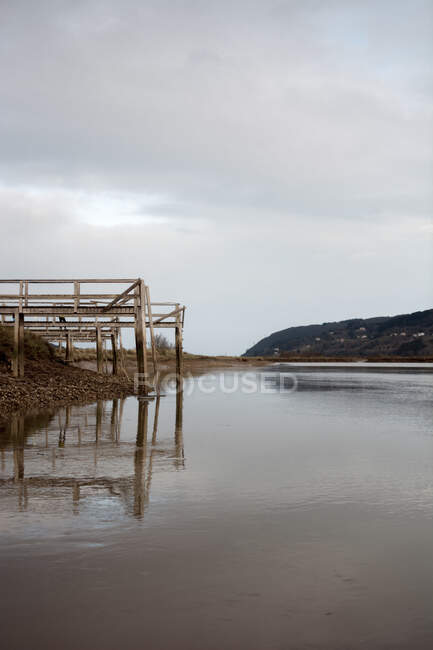 Alter Holzsteg am Ufer in der Nähe ruhigen Wassers an bewölkten Tag in der Landschaft — Stockfoto