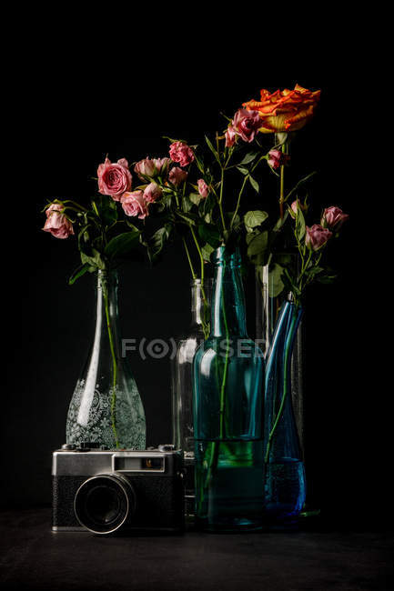 Cámara de fotos vintage y jarrones de vidrio con ramos de flores encantadoras sobre fondo negro — Stock Photo