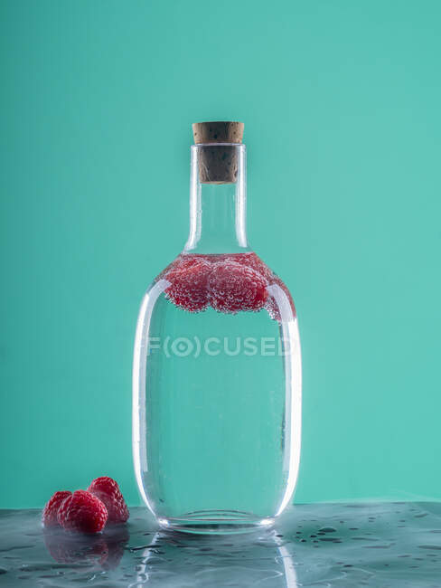 Glass bottle with blue beverage near berries on board on abstract background — Stock Photo