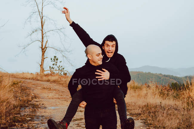 Felice coppia omosessuale divertirsi sulla strada tra le piante in montagna — Foto stock