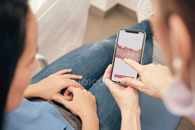Female dentist demonstrating smartphone with teeth scan to woman in clinic — Stock Photo