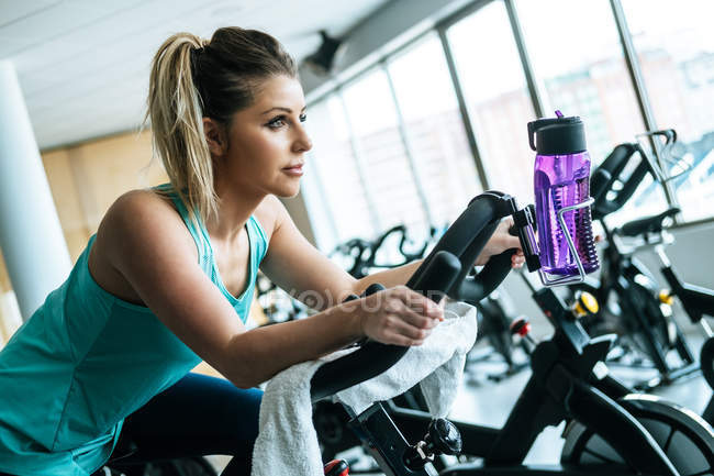 Mujer con toalla y agua en máquina de ejercicios en el gimnasio - foto de stock
