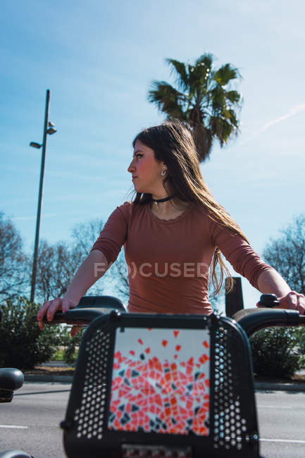 Jeune jolie femme chevauchant de retour sur scooter sur le parking dans la journée ensoleillée — Photo de stock