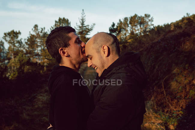 Feliz casal homossexual abraçando na floresta em dia ensolarado — Fotografia de Stock