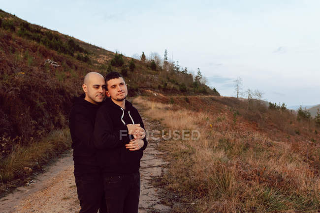 Casal homossexual sonhador abraçando na rota na natureza — Fotografia de Stock