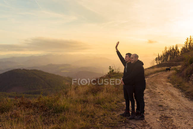Seitenansicht eines homosexuellen Paares, das sich auf der Strecke in der Dunkelheit umarmt und malerischer Blick auf das Tal im Nebel — Stockfoto