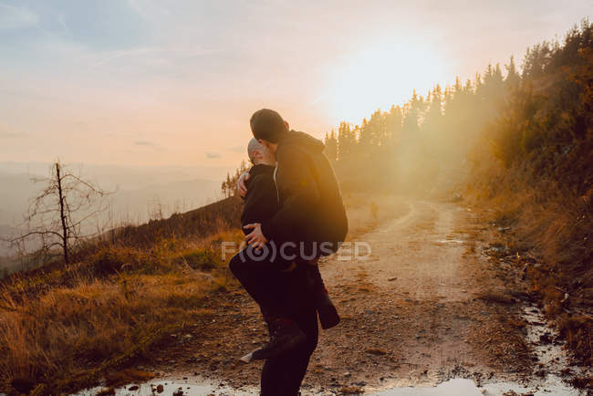 Happy homosexual couple having fun on route between plants on mountain and blue sky — Stock Photo