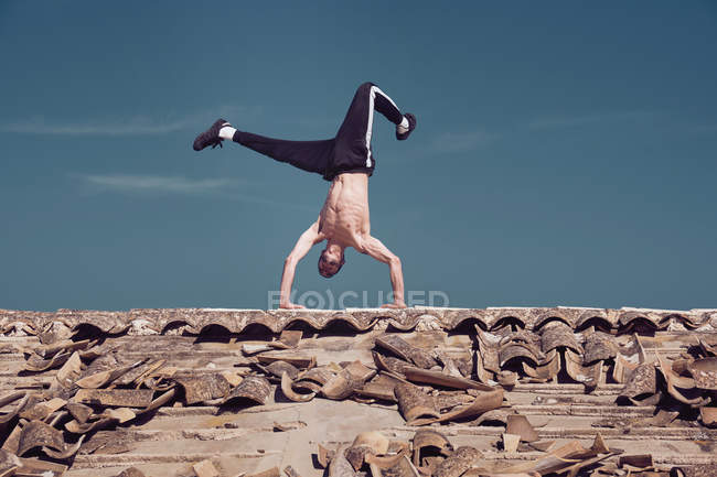 Mann macht Handstand auf Dach vor blauem Himmel — Stockfoto