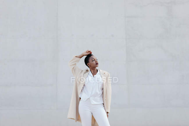 Modelo de pelo corto de moda en traje blanco posando contra pared gris - foto de stock